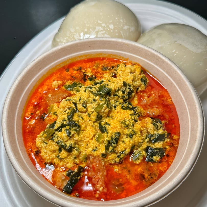 Nigerian Egusi soup with red stew and green vegetables, served with two mounds of pounded yam.