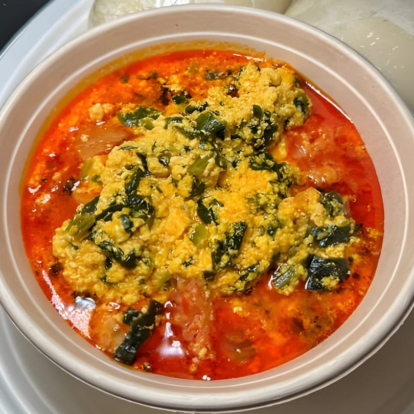 A bowl of Nigerian Egusi soup with a vibrant red base and yellow-green mixture on top.