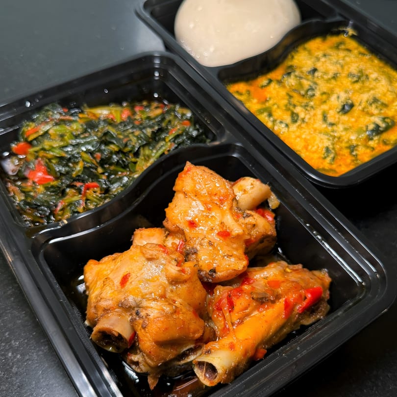 Nigerian meal in a black takeout container with stewed chicken, greens, and fufu.