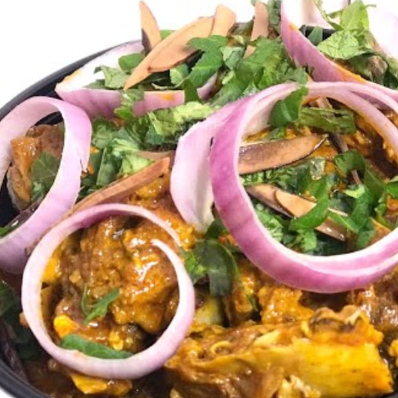 A close-up of Nigerian goat meat pepper soup, garnished with red onion rings and green herbs.
